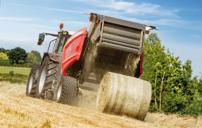 Round Baler ejecting a bale on uneven ground.